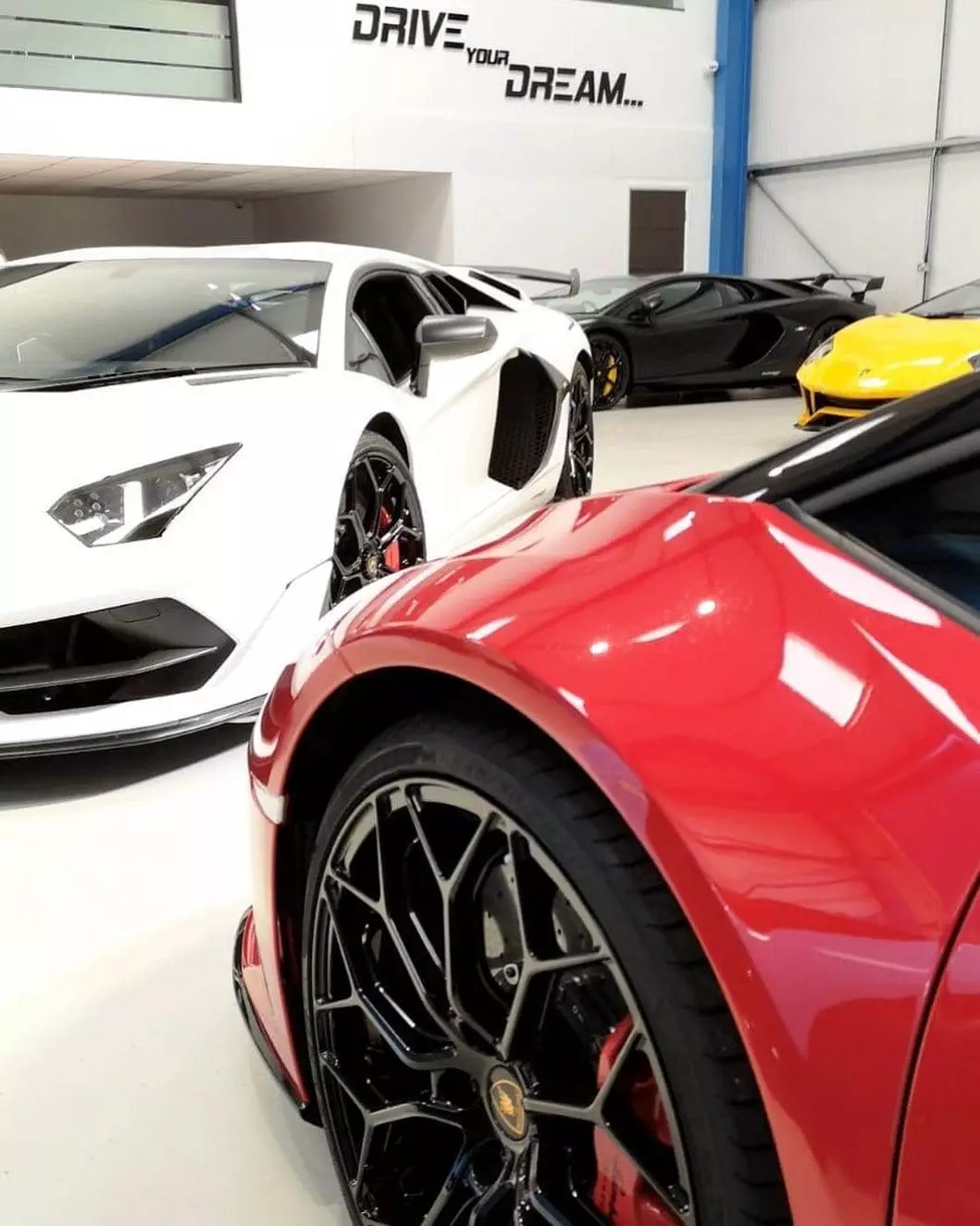 Luxury sports cars, including a red, white, and yellow model, parked in a showroom with 
