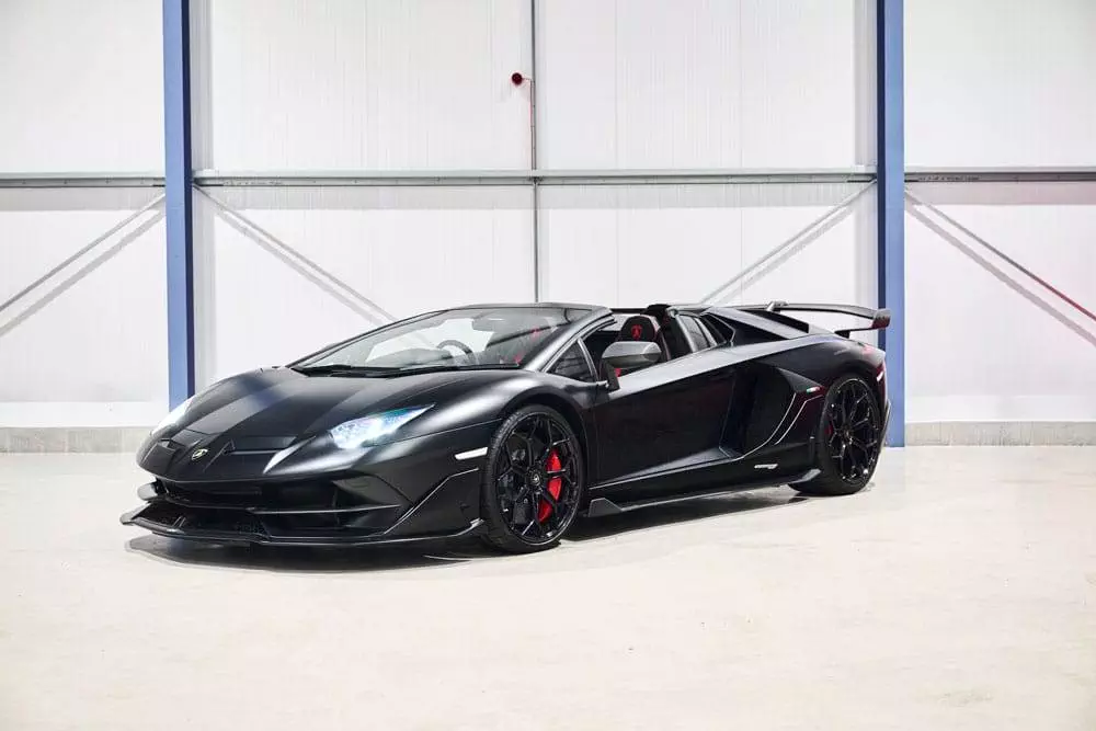 Black lamborghini aventador with doors open parked inside a white industrial building.