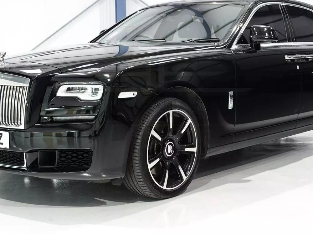 A black rolls-royce parked in a well-lit showroom, featuring a sleek exterior and distinctive front grille.